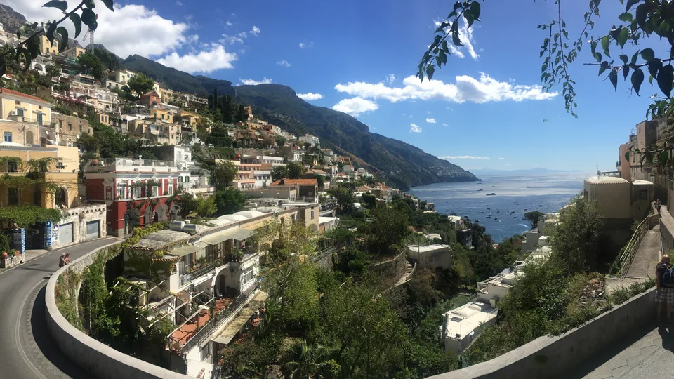 Positano’s pastel buildings and curving coastal road descending toward a bright blue Mediterranean