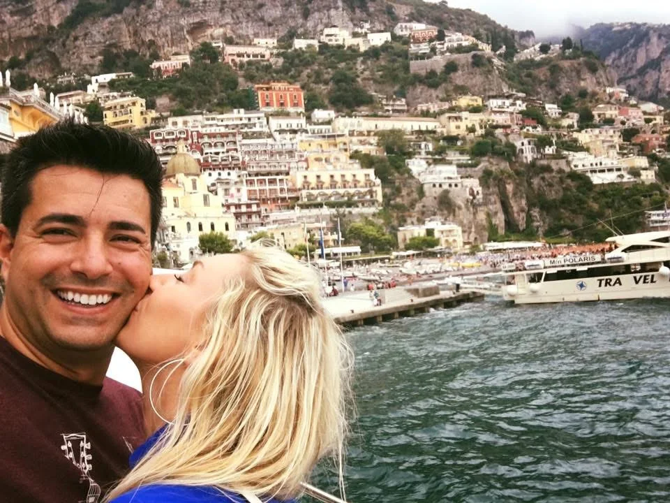 Kristin beijando Alex no rosto num barco junto à orla de Positano