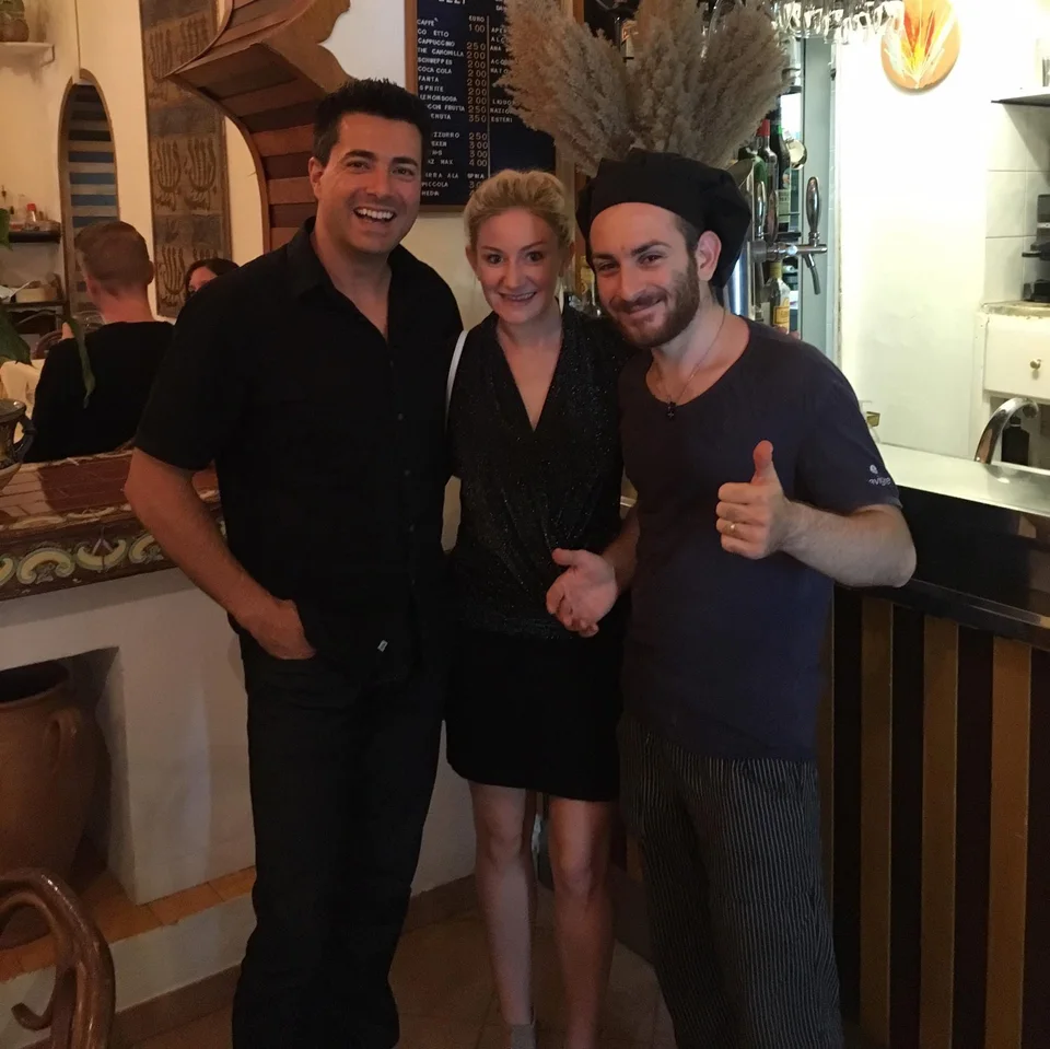 Alex e Kristin sorrindo ao lado de um integrante da equipe da cozinha de um restaurante