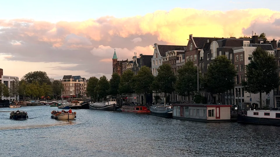 Casas à beira de um canal de Amsterdã sob o céu rosa e dourado do entardecer