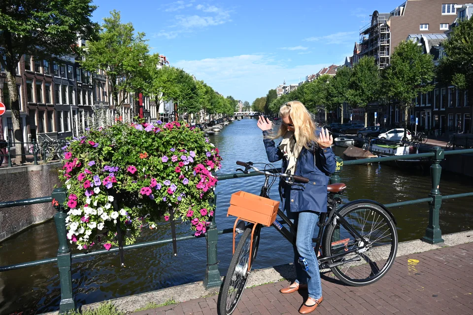 Kristin com uma bicicleta laranja ao lado das flores de um canal