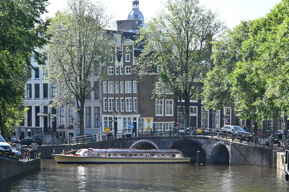 Uma casa à beira do canal atrás de uma ponte de pedra e árvores