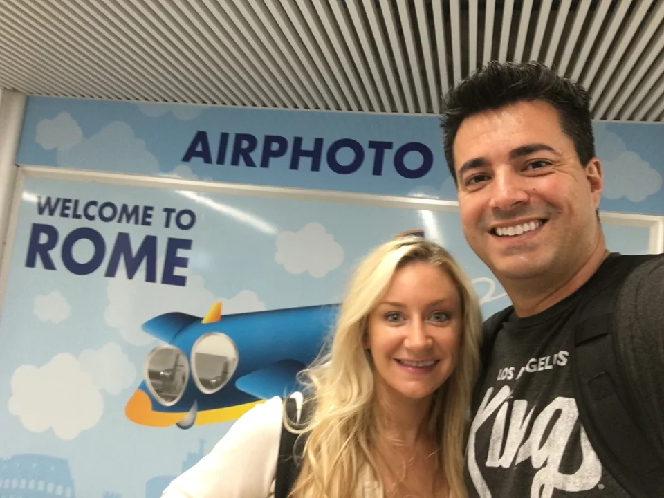 Alex and Kristin in front of an airport Welcome to Rome sign
