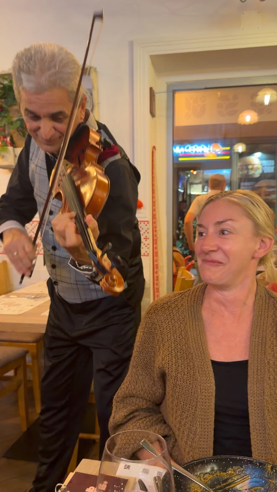 Um violinista tocando ao lado de Kristin à mesa de um restaurante