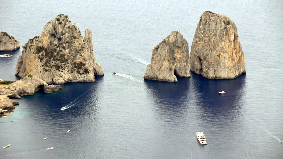 A high view of Capri’s Faraglioni surrounded by deep blue sea and small boats