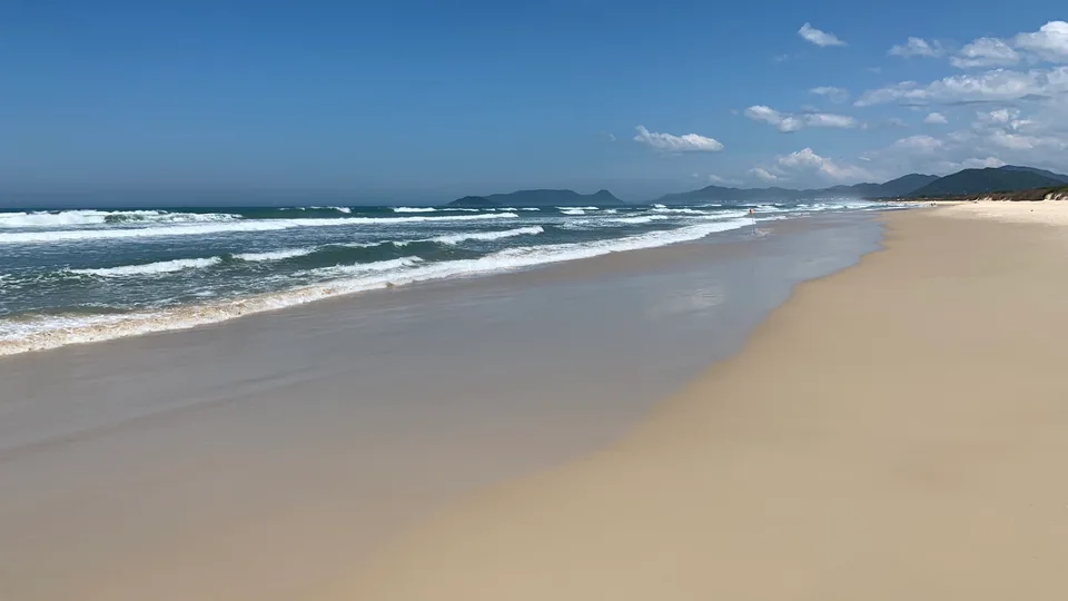 A long sweep of Joaquina beach with white waves and wet sand