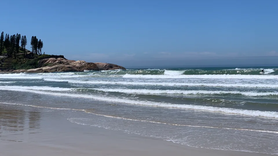White surf rolling toward Joaquina’s sand and shoreline rocks
