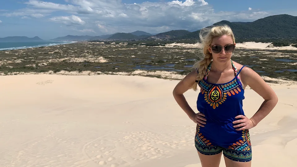 Kristin standing among pale coastal dunes with green hills behind