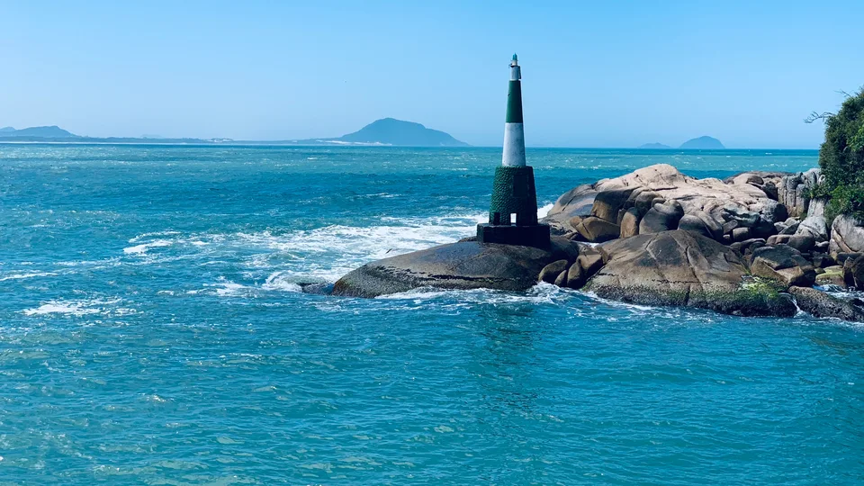 A navigation beacon beside blue water and shoreline rocks at Barra da Lagoa