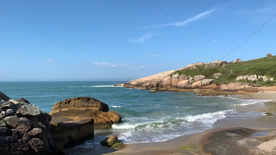 Shoreline rocks, pale sand and blue water along Florianópolis’s eastern coast