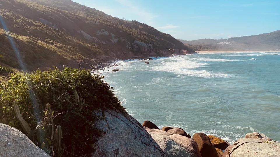 A sunlit coastal view with green slopes and white surf
