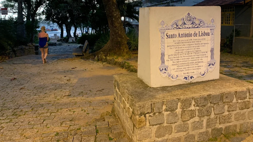 Kristin walking along a stone path beside a Santo Antônio de Lisboa heritage plaque