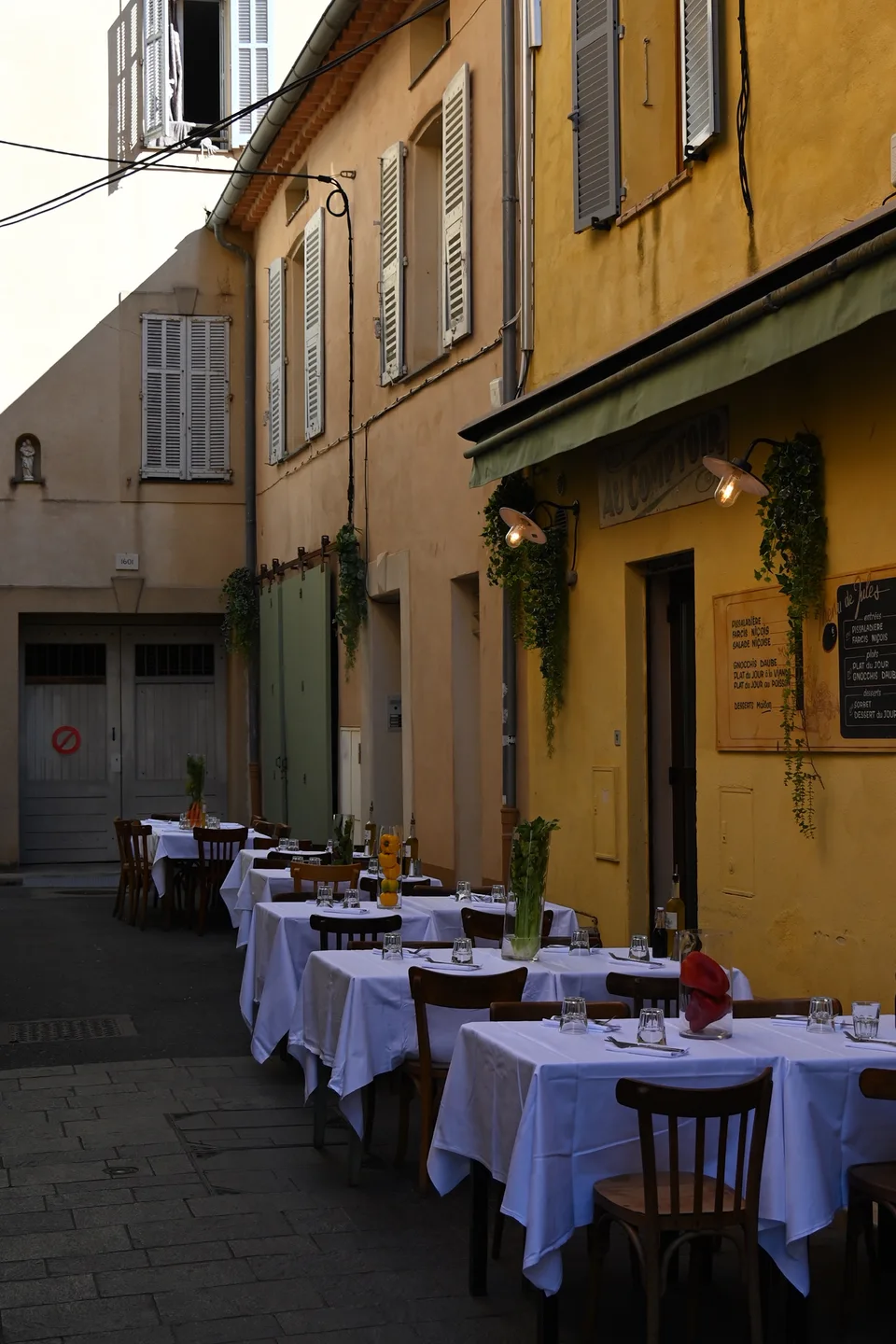 Restaurant tables arranged along a shaded Riviera lane