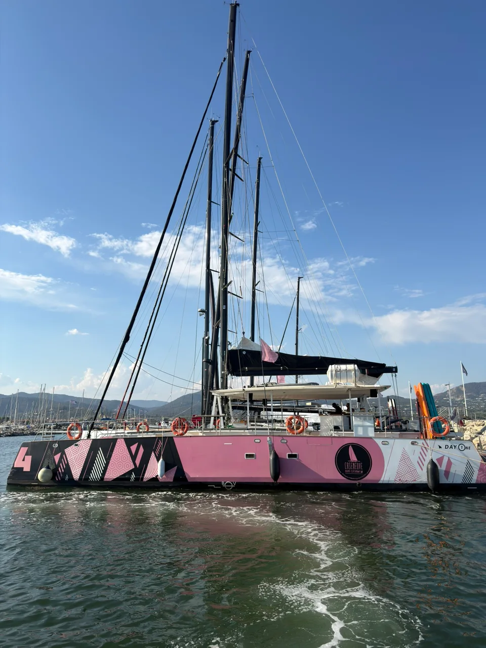 A pink-hulled sailing boat moored in the harbor