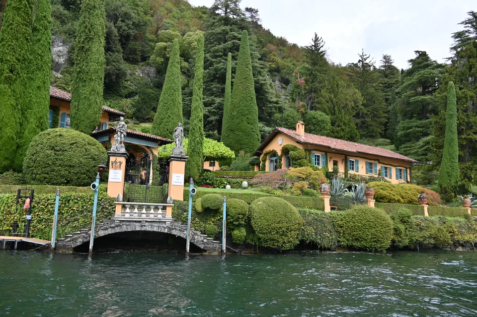 Ciprestes altos e cercas-vivas aparadas junto a uma villa à beira do lago