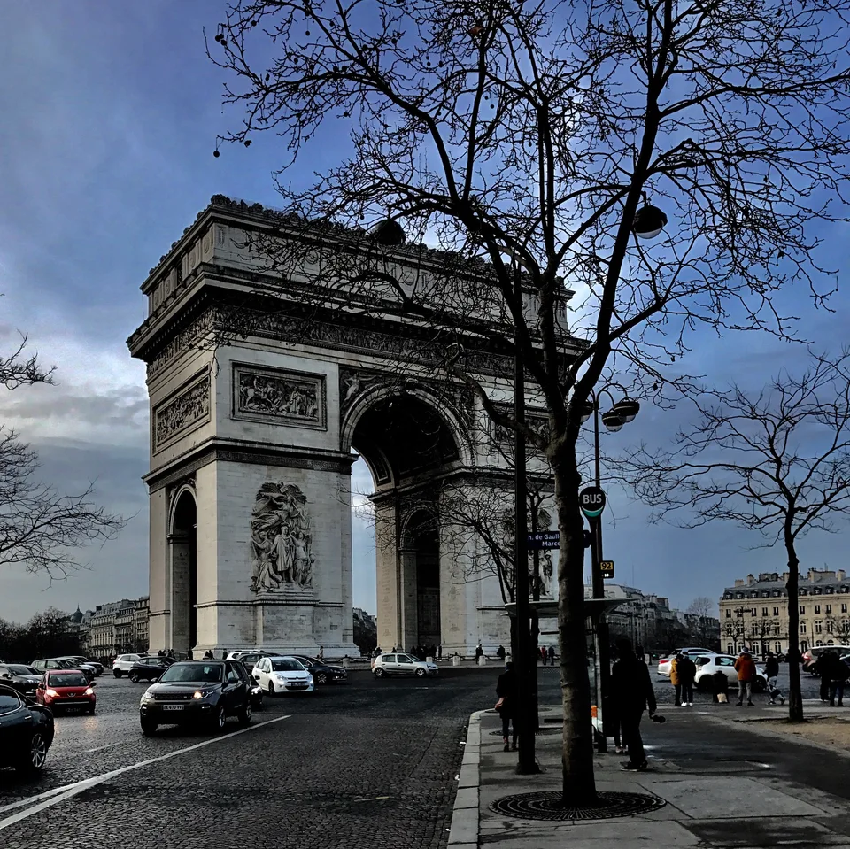 O Arco do Triunfo visto entre árvores sem folhas a partir da avenida ao redor