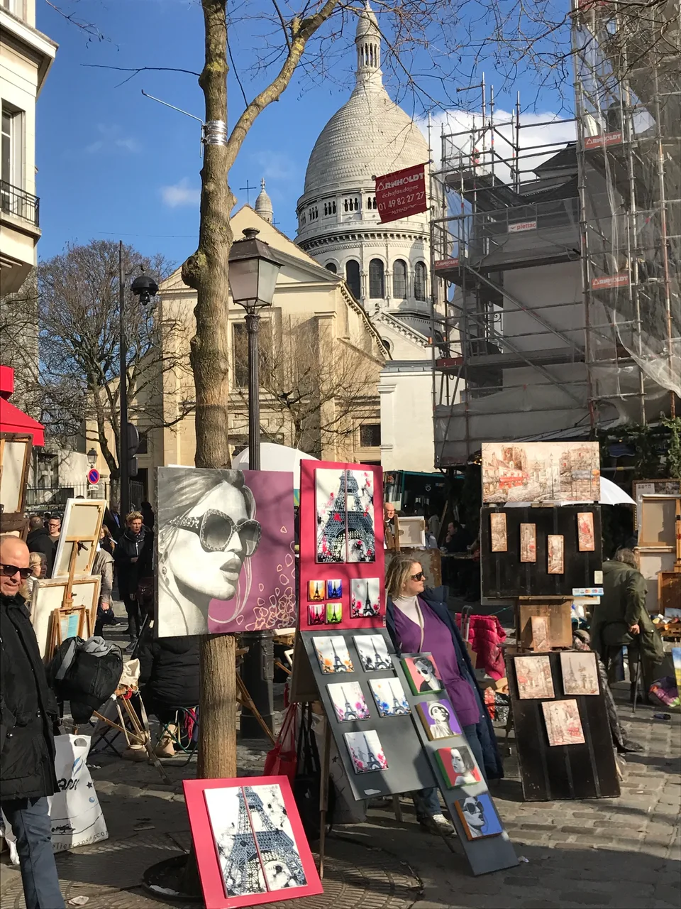 Pinturas emolduradas ao lado de uma árvore sem folhas e prédios de pedra em Montmartre