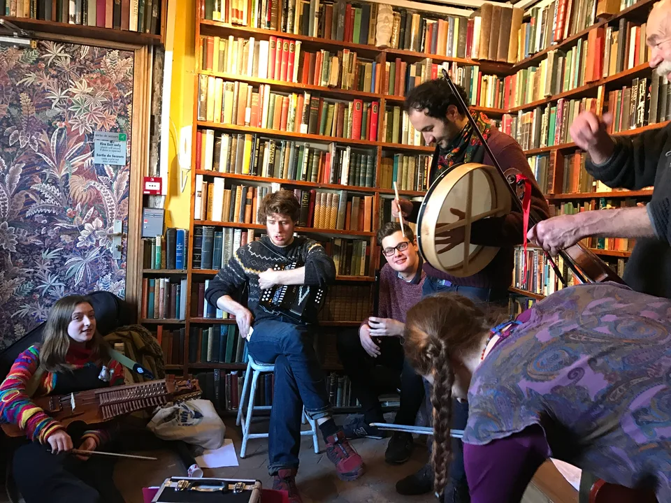 Músicos tocando instrumentos de cordas entre as estantes da Shakespeare and Company