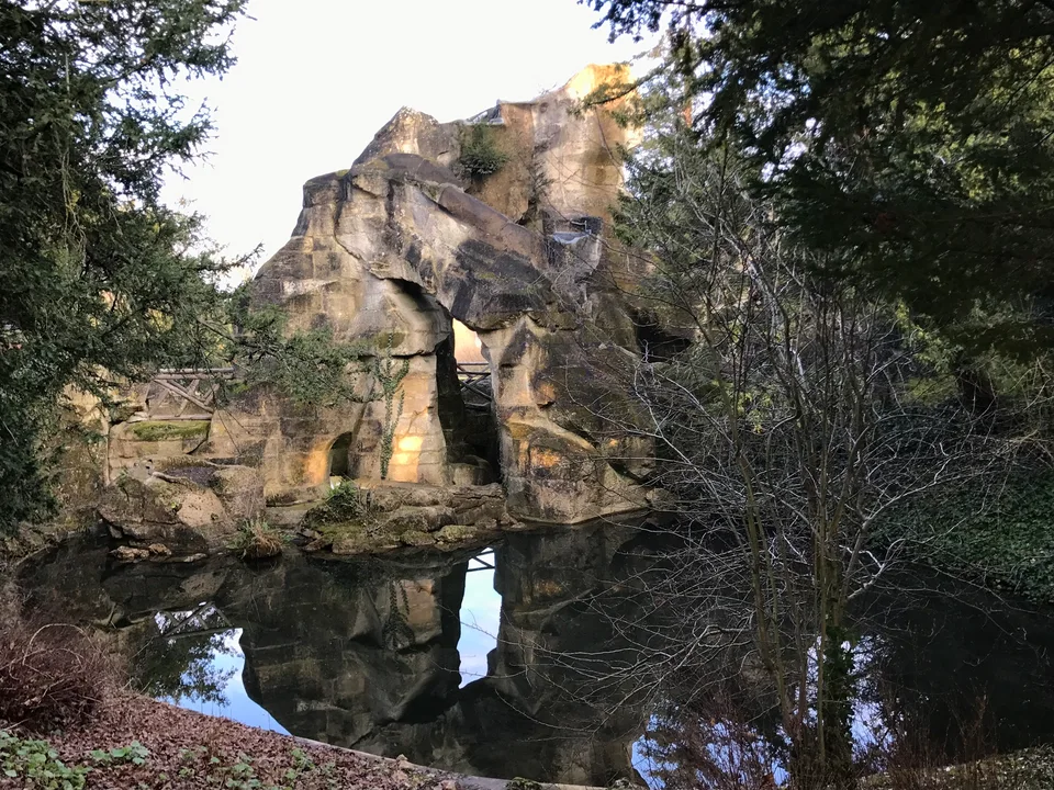 Uma gruta de pedras e um lago sob galhos inclinados nos jardins de Versalhes