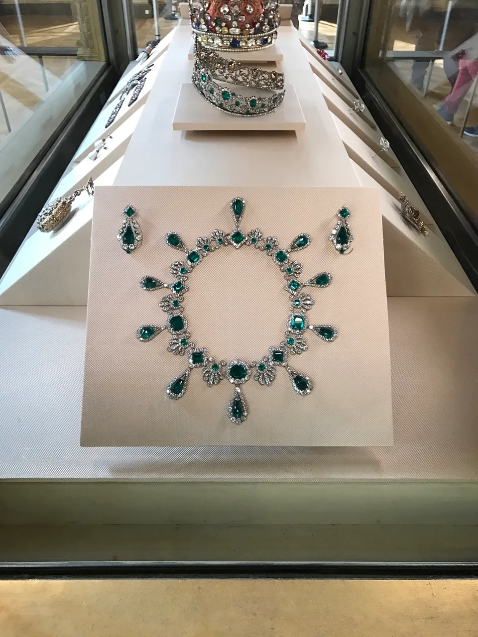 Um colar de pedras verdes e diamantes numa vitrine branca de museu