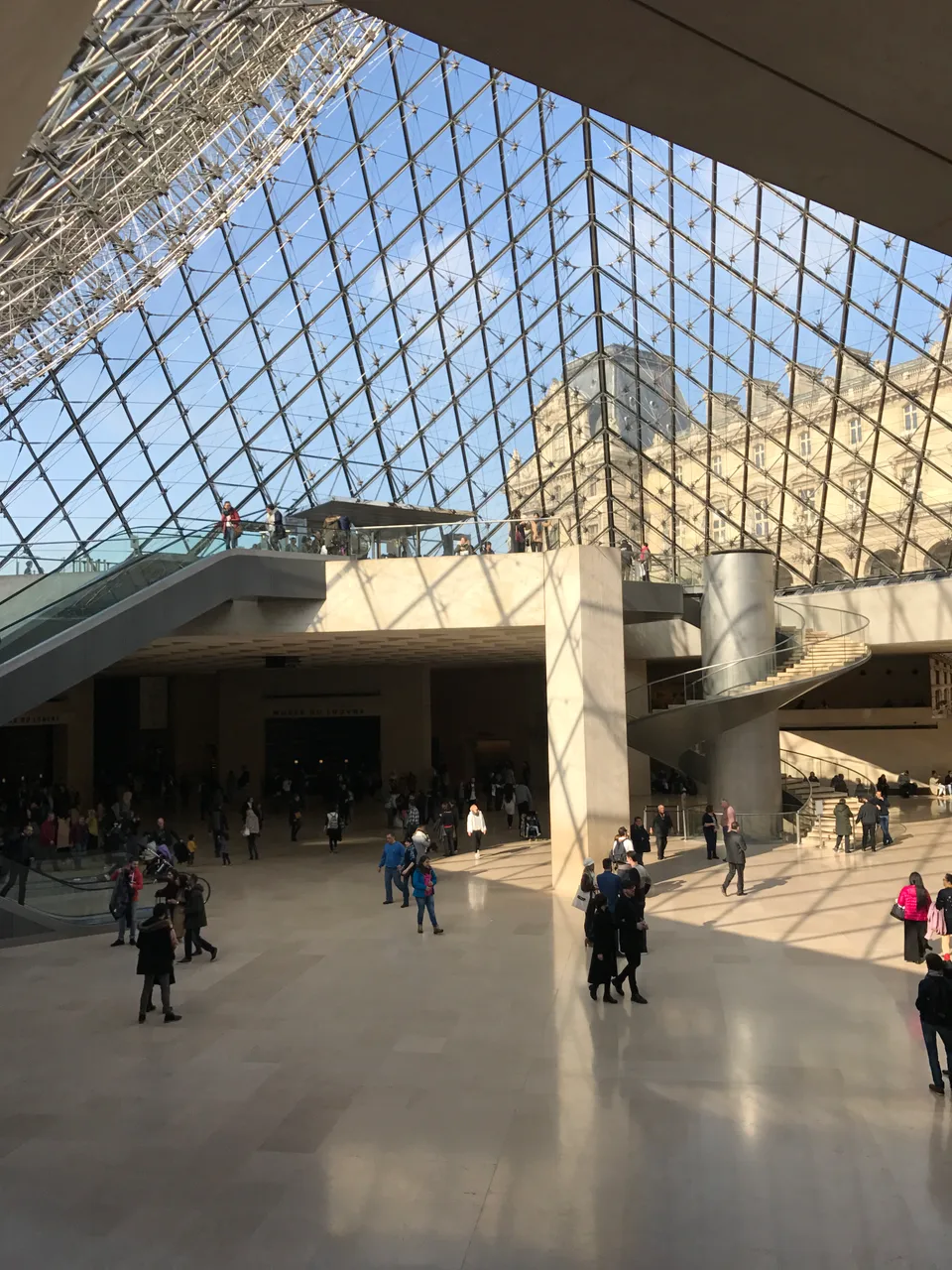 Sunlight filtering through the glass pyramid into the Louvre entrance hall