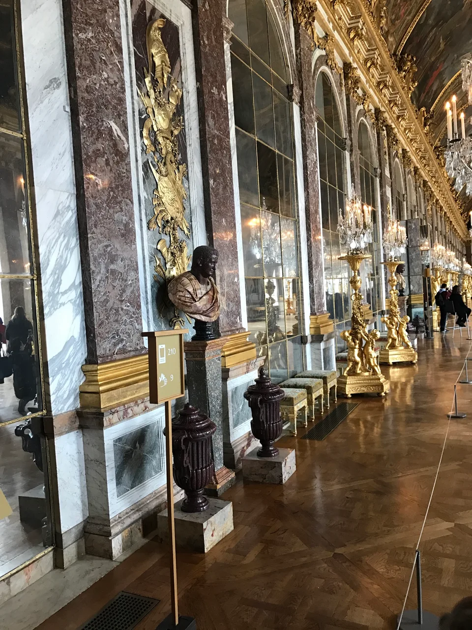 A longa Galeria dos Espelhos em Versalhes com lustres, arcos dourados e visitantes