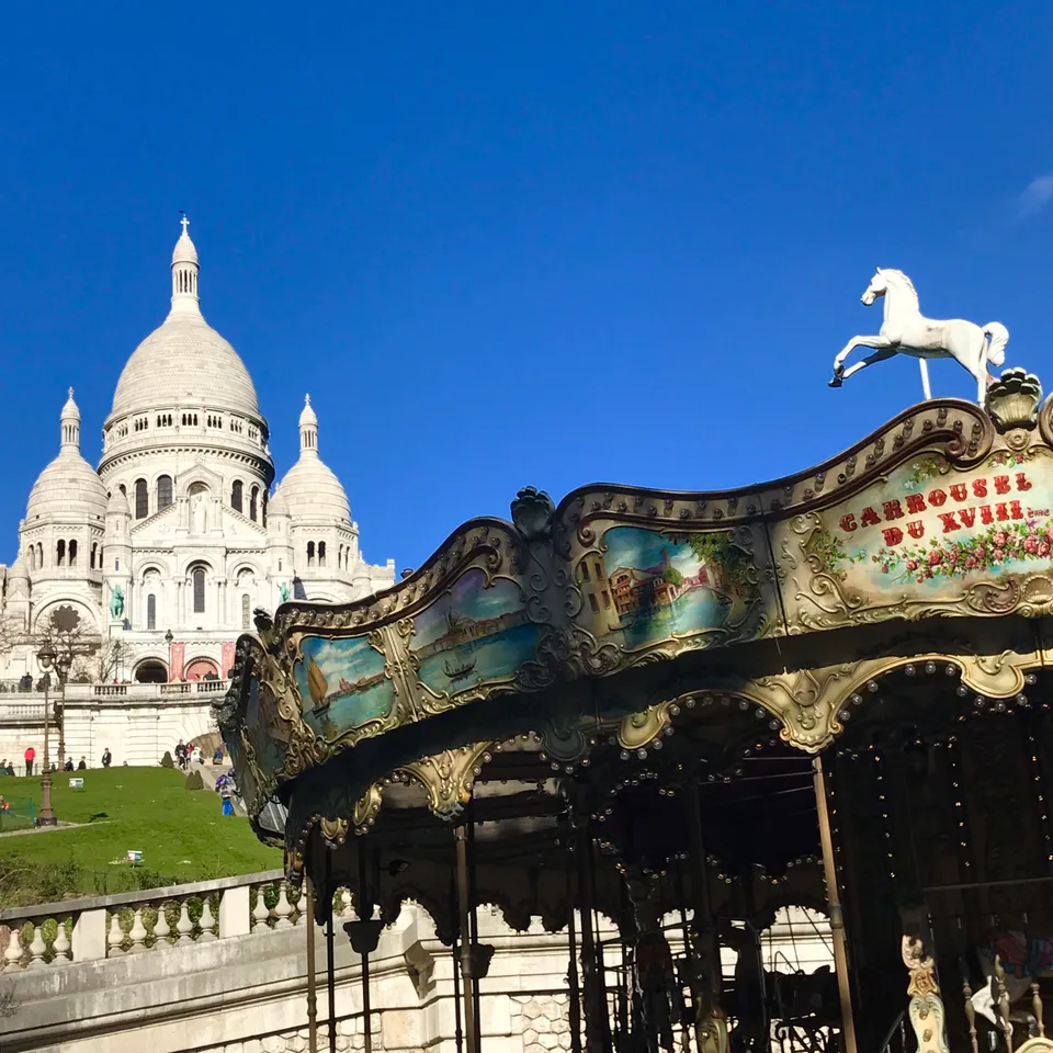 A carousel below the white domes of Sacré-Cœur in Montmartre beneath a clear blue sky