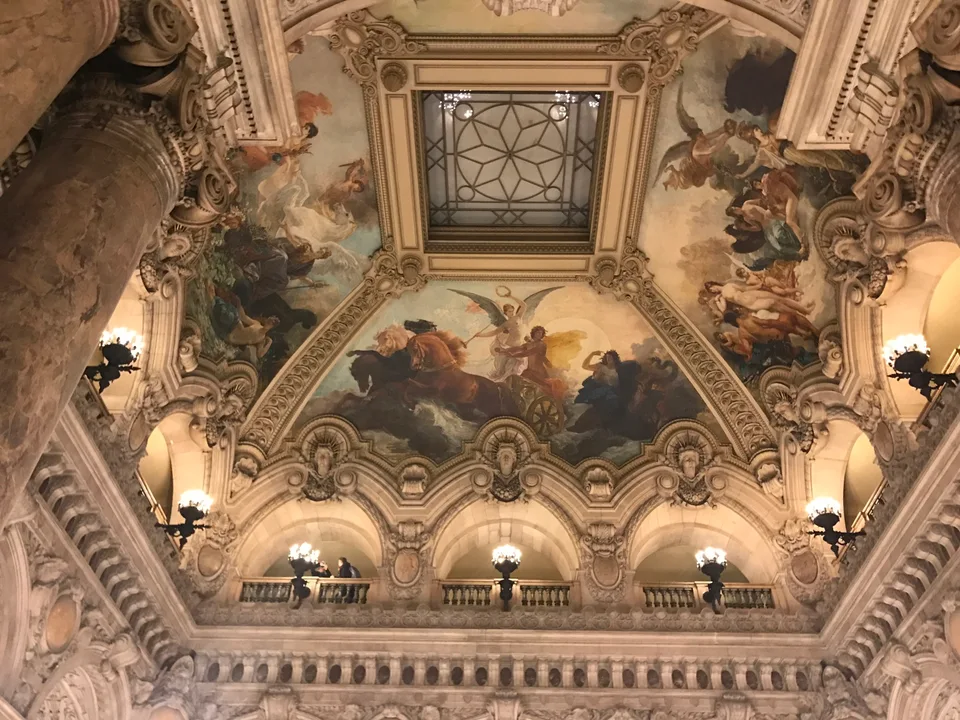 Painéis pintados no teto, esculturas e arcos ornamentados sobre a escadaria do Palais Garnier