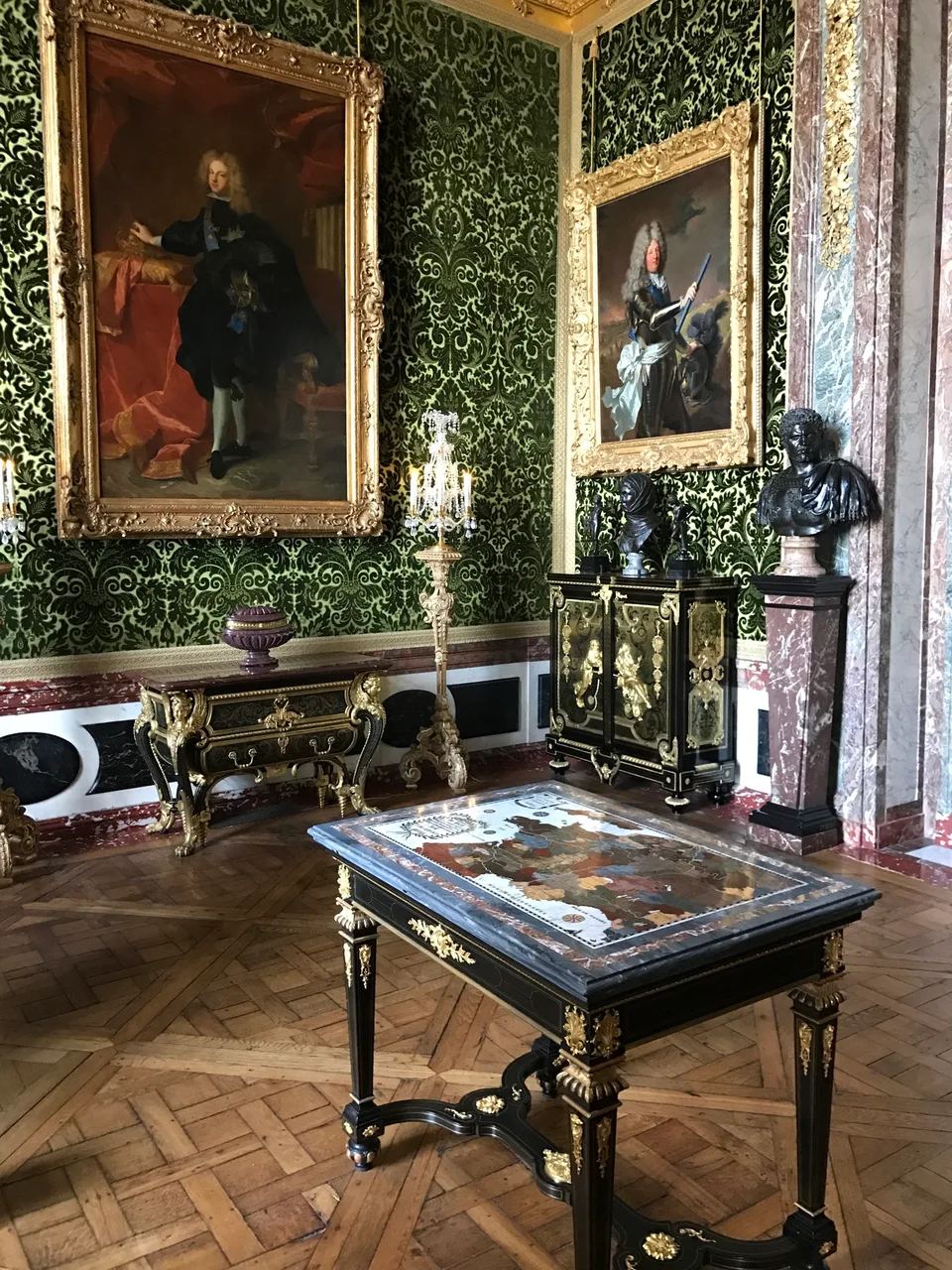 Um salão ornamentado de Versalhes com pinturas, espelhos dourados e uma escrivaninha