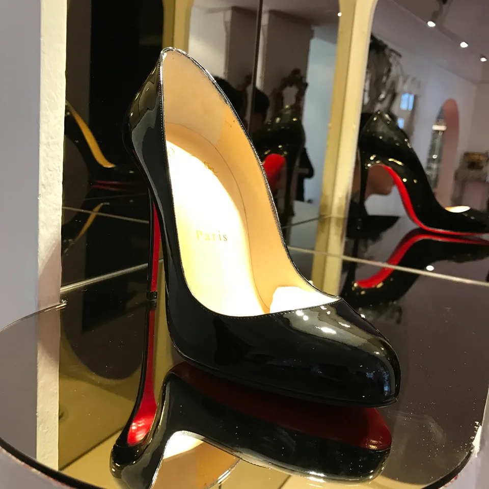 Sapatos Christian Louboutin de verniz preto e sola vermelha numa vitrine de butique