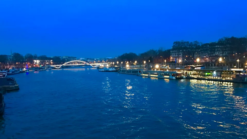 O Sena na hora azul com margens iluminadas e uma ponte ao longe