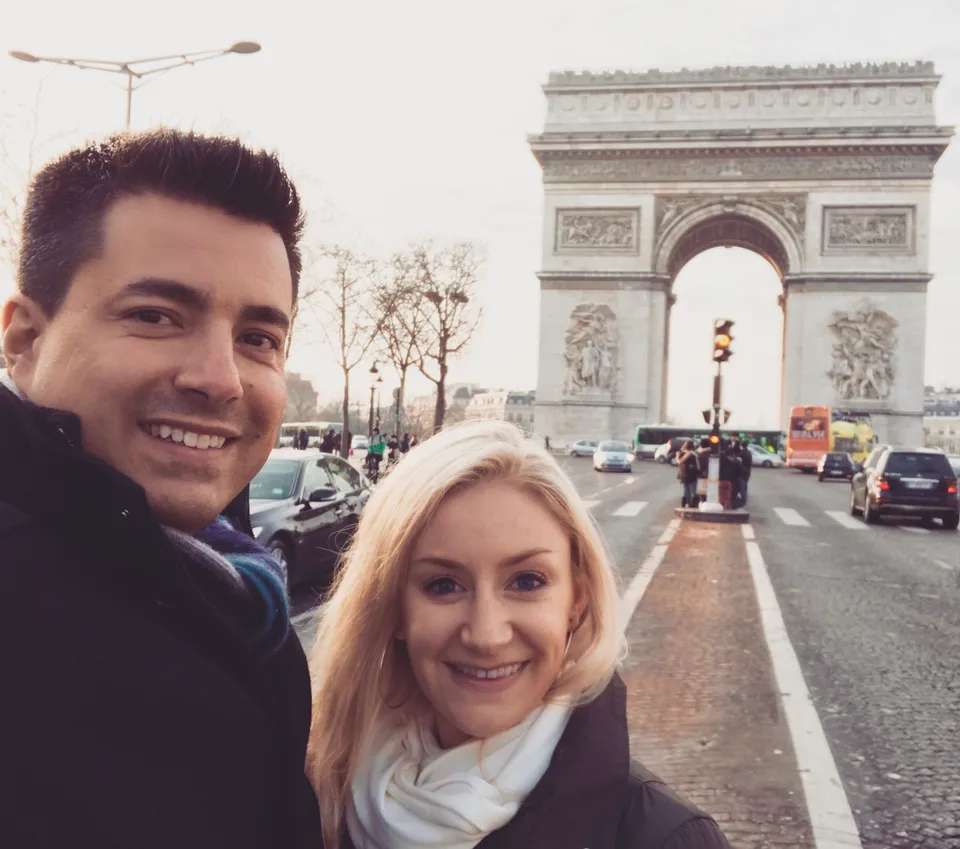 Alex and Kristin wearing coats and scarves in front of the Arc de Triomphe