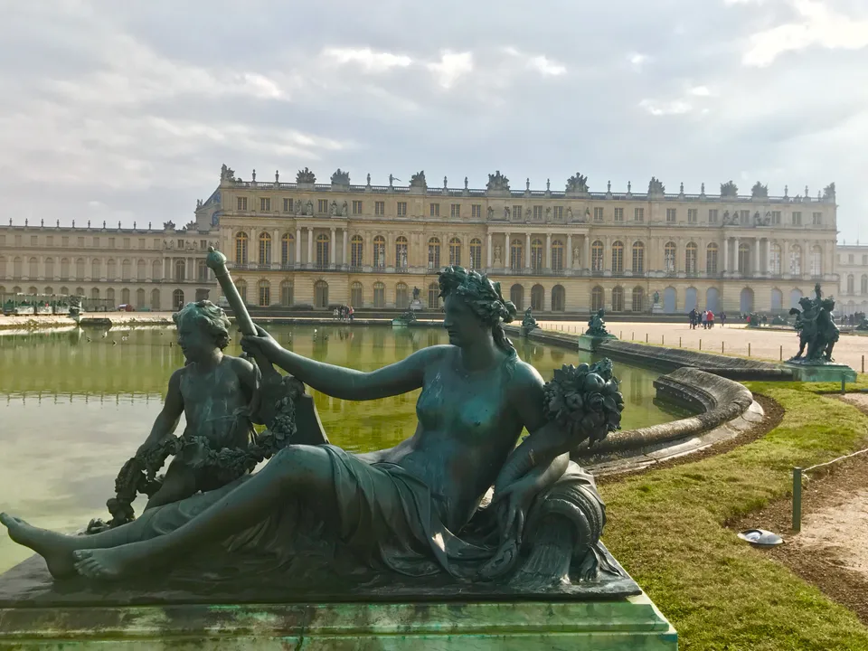 Bronze fountain figures and a broad pool in front of the Palace of Versailles in winter