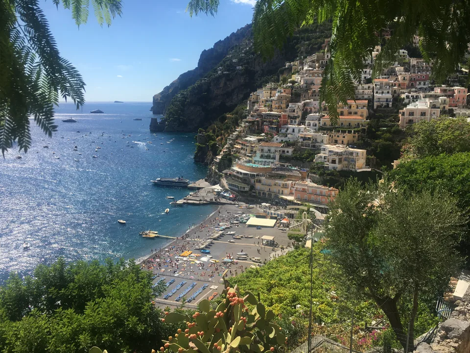 Positano’s waterfront and steep green hillside beside a wide expanse of blue sea