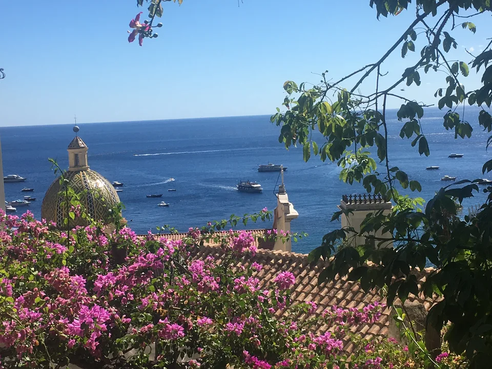 Pink bougainvillea and the tiled dome of Santa Maria Assunta above the sea in Positano