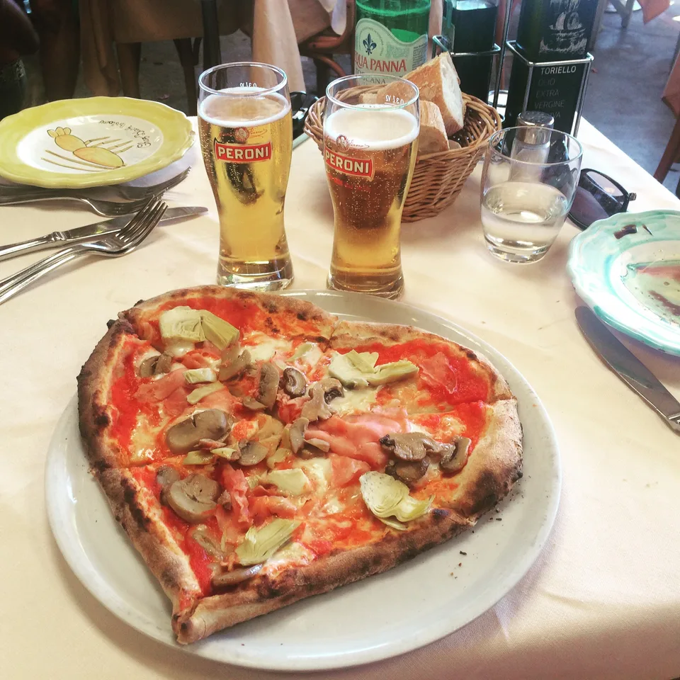 A pizza with tomatoes and basil on a small restaurant table with drinks