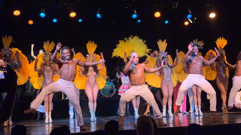 Dancers in colorful costumes and feathered headdresses across a stage