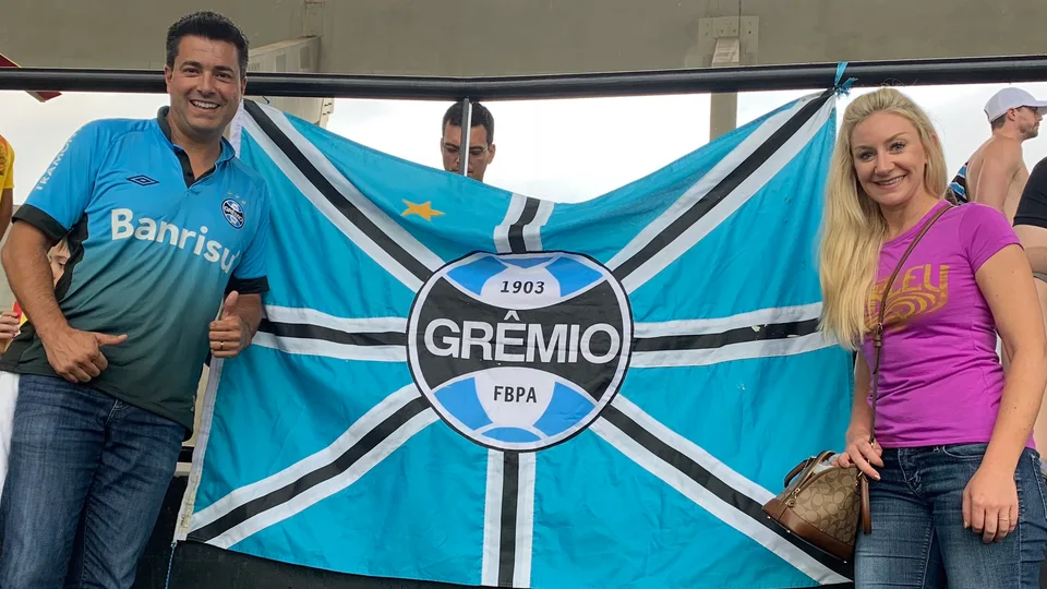 Alex and Kristin holding a Grêmio flag in the stadium stands