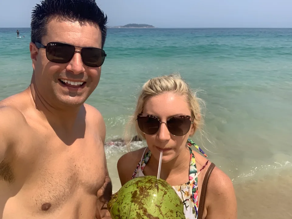 Alex and Kristin standing together in the shallow sea with a green coconut
