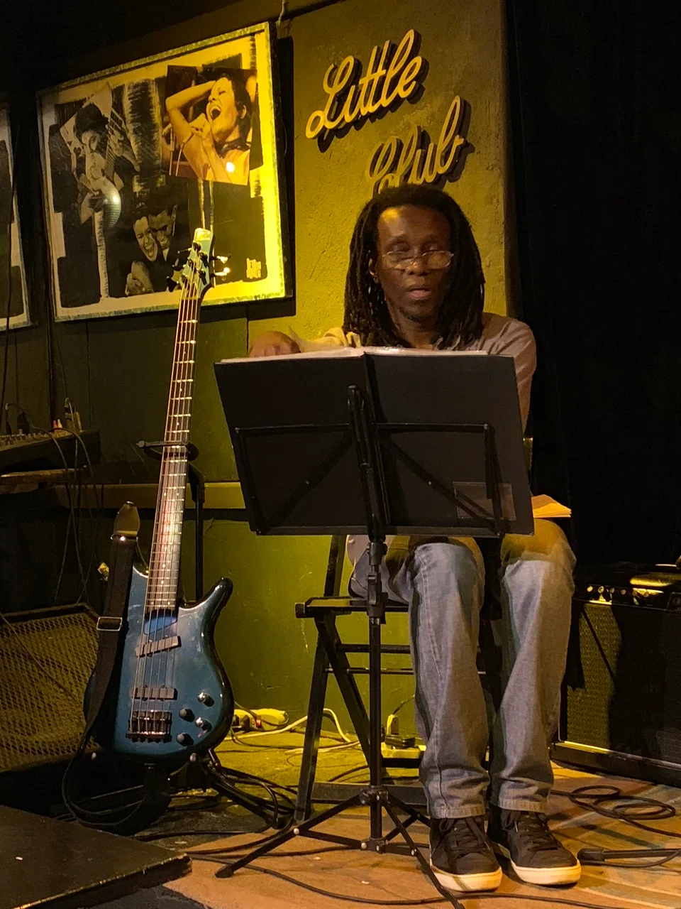 A singer at a microphone beneath framed photographs in the Little Club