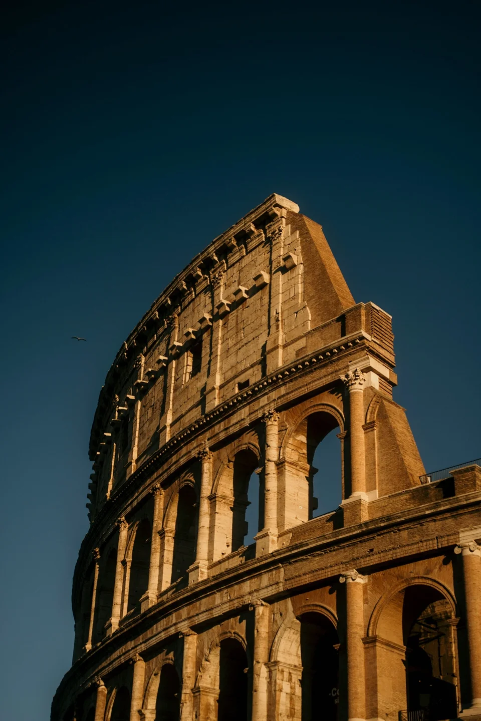Sunlit arches of the Colosseum rising against a deep blue sky