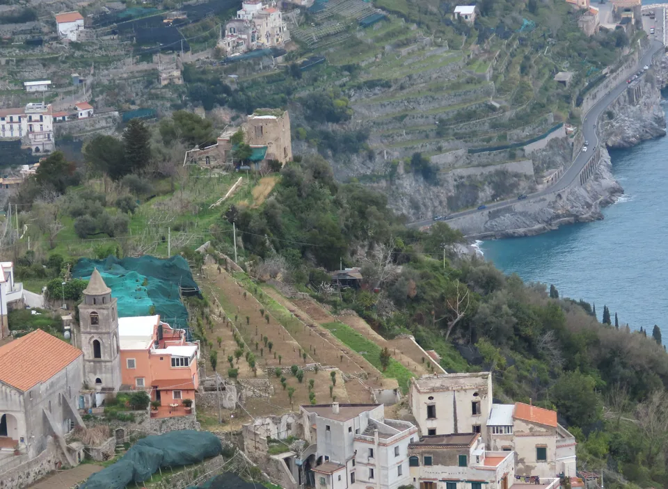 Uma estrada estreita serpenteando por uma encosta íngreme da Costa Amalfitana entre terraços cultivados e casas
