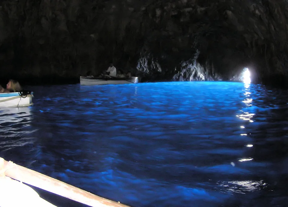 Barcos a remo na Gruta Azul de Capri sobre água azul intensa iluminada pela entrada