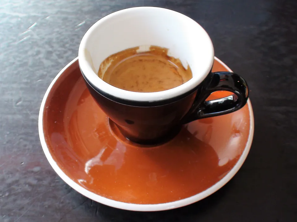 Um espresso numa xícara preta sobre um pires cor de terracota