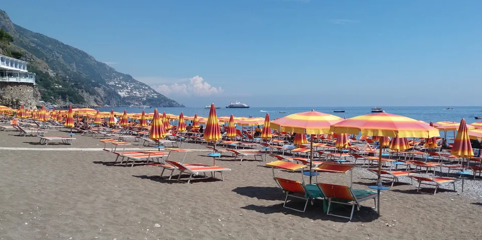 Guarda-sóis laranjas e amarelos e espreguiçadeiras na Spiaggia Grande de Positano, junto ao mar azul