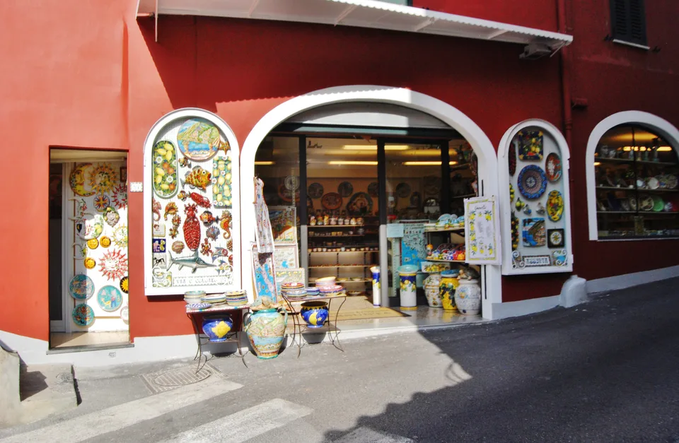 Pratos e peças de cerâmica coloridos ao redor da entrada vermelha de uma loja em Positano