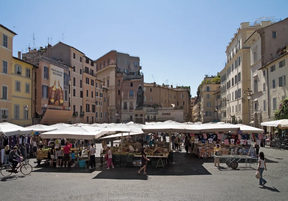 Toldos brancos e bancas de produtos sob a estátua de Giordano Bruno no Campo de’ Fiori
