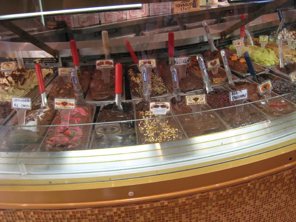 Fileiras de sabores de gelato atrás do balcão curvo de vidro de uma gelateria romana